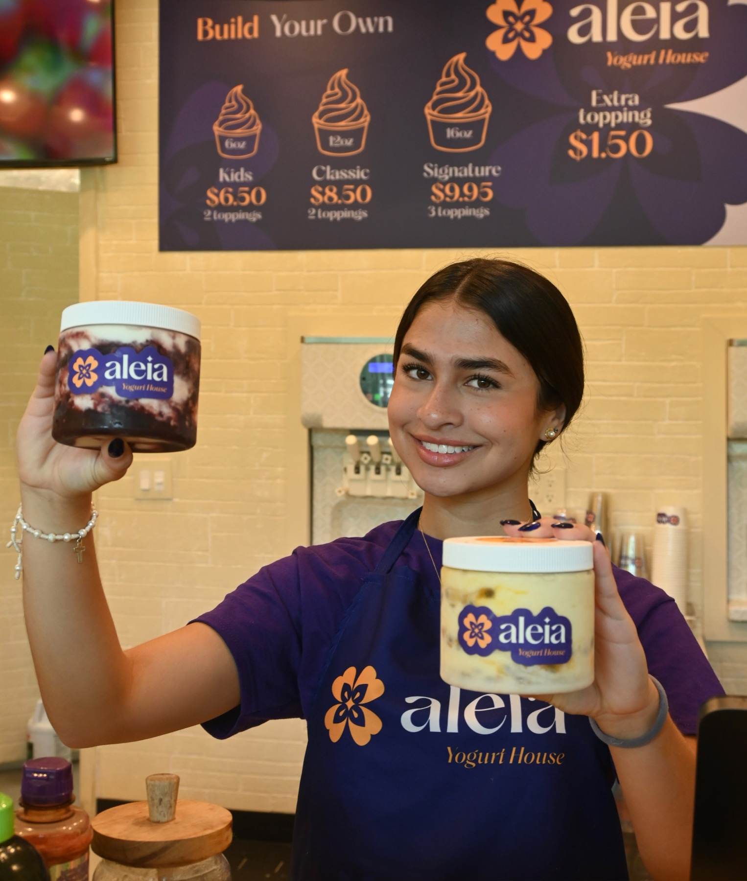 An aleia team member in her purple apron smiling and holding up two pints of frozen yogurt