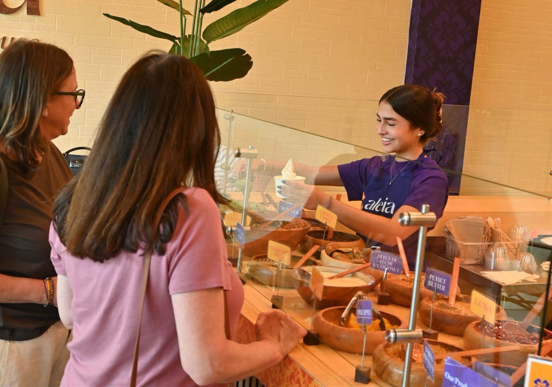 An aleia team member handing a cup of frozen yogurt to guests across the toppings bar